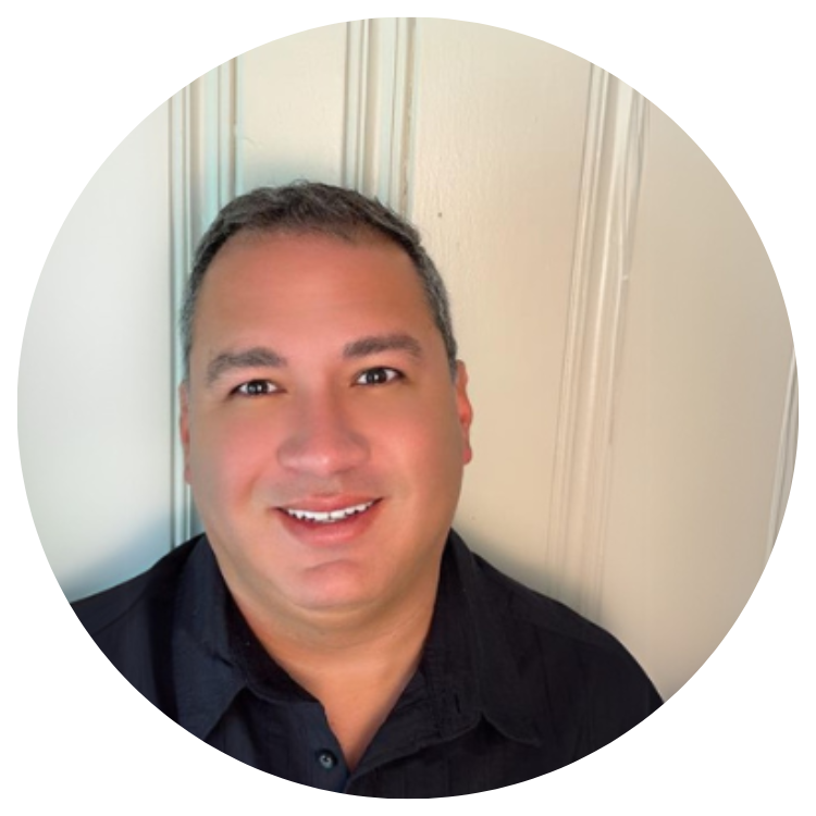 Man with short brown hair smiles, wearing a black shirt, in front of a white door.