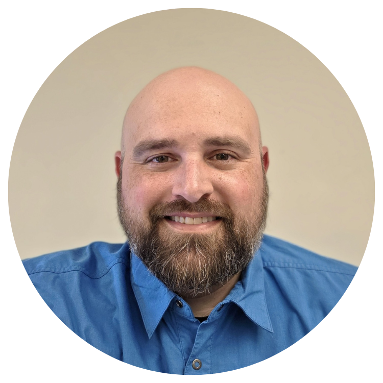 Bald man with a full beard smiles, wearing a blue collared shirt.
