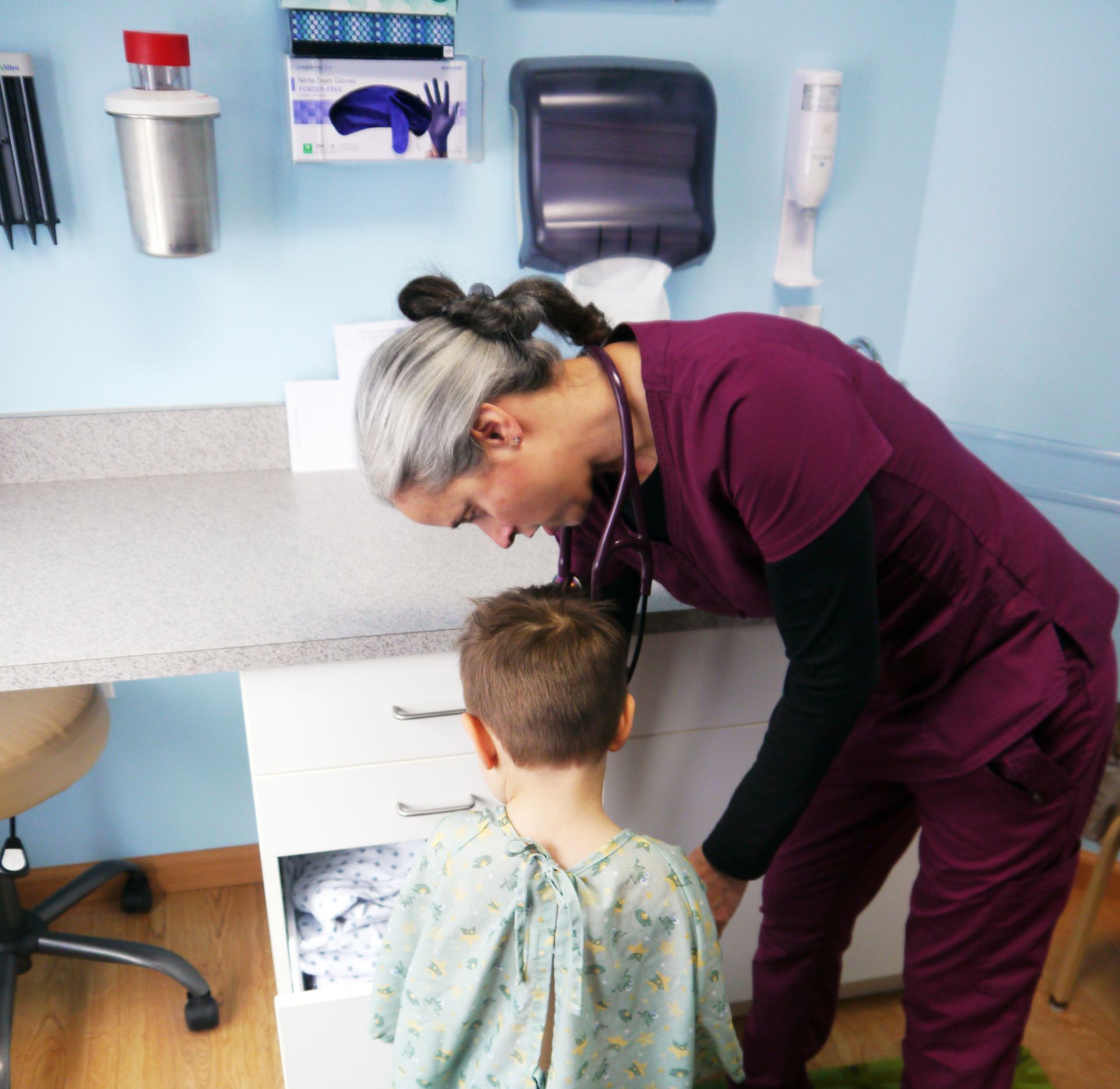 A woman in purple scrubs is talking to a young boy in a hospital gown.