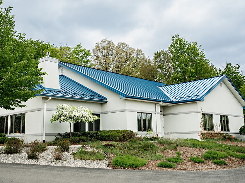 White building with blue roof surrounded by bushes and trees.