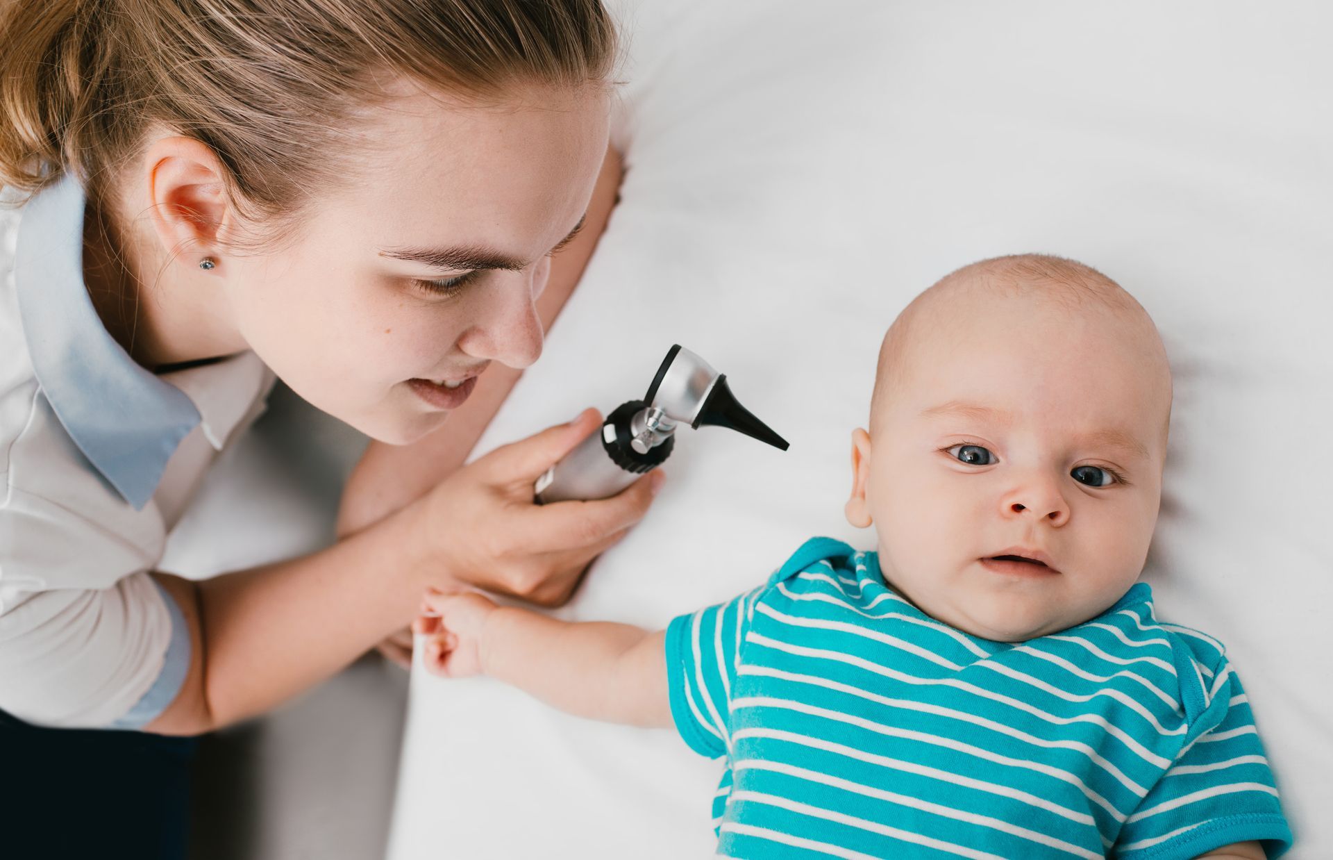 A female pediatrician is using an otoscope to look into a baby's ear.