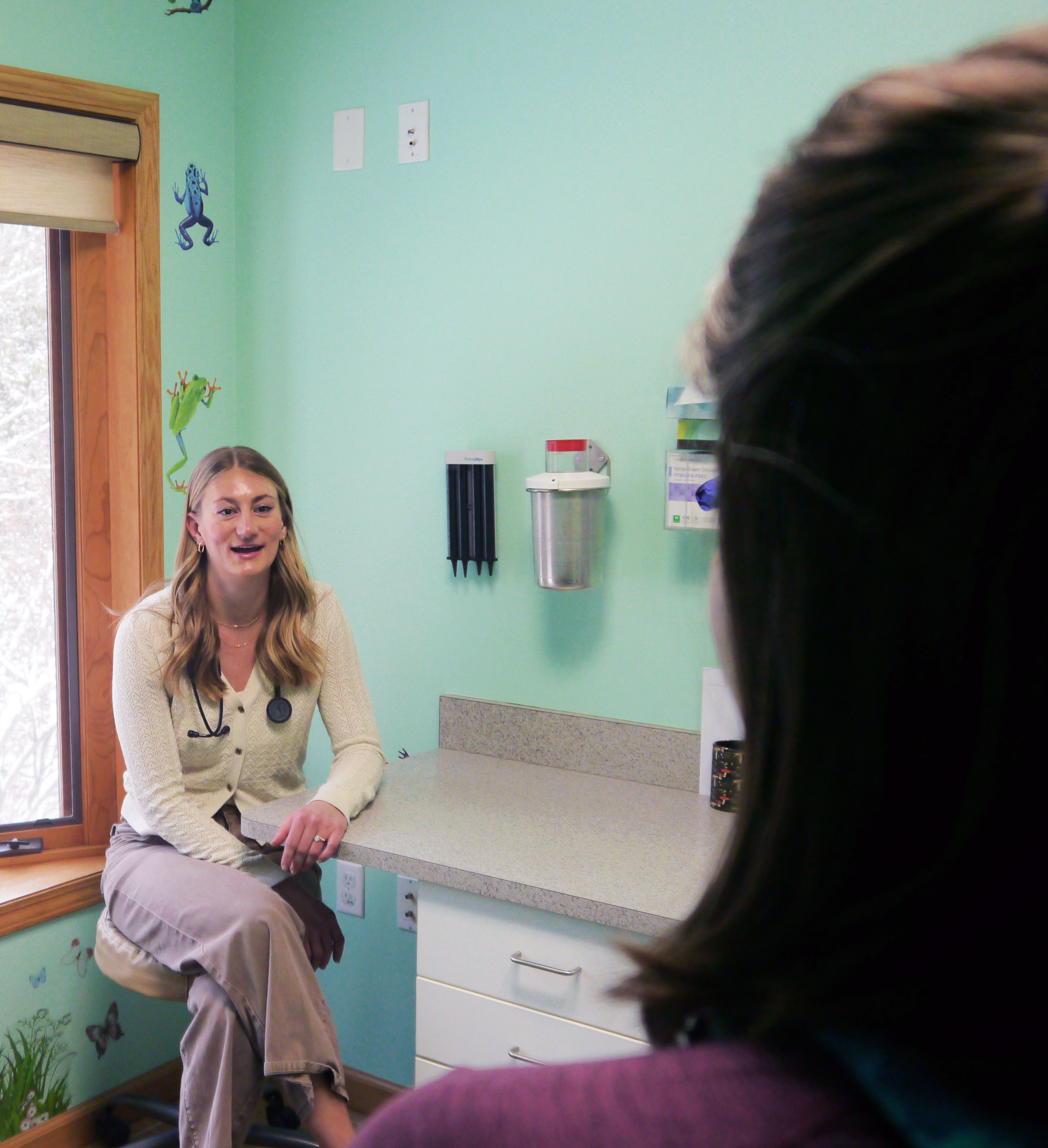 Medical professional sitting on a chair in a medical exam room.
