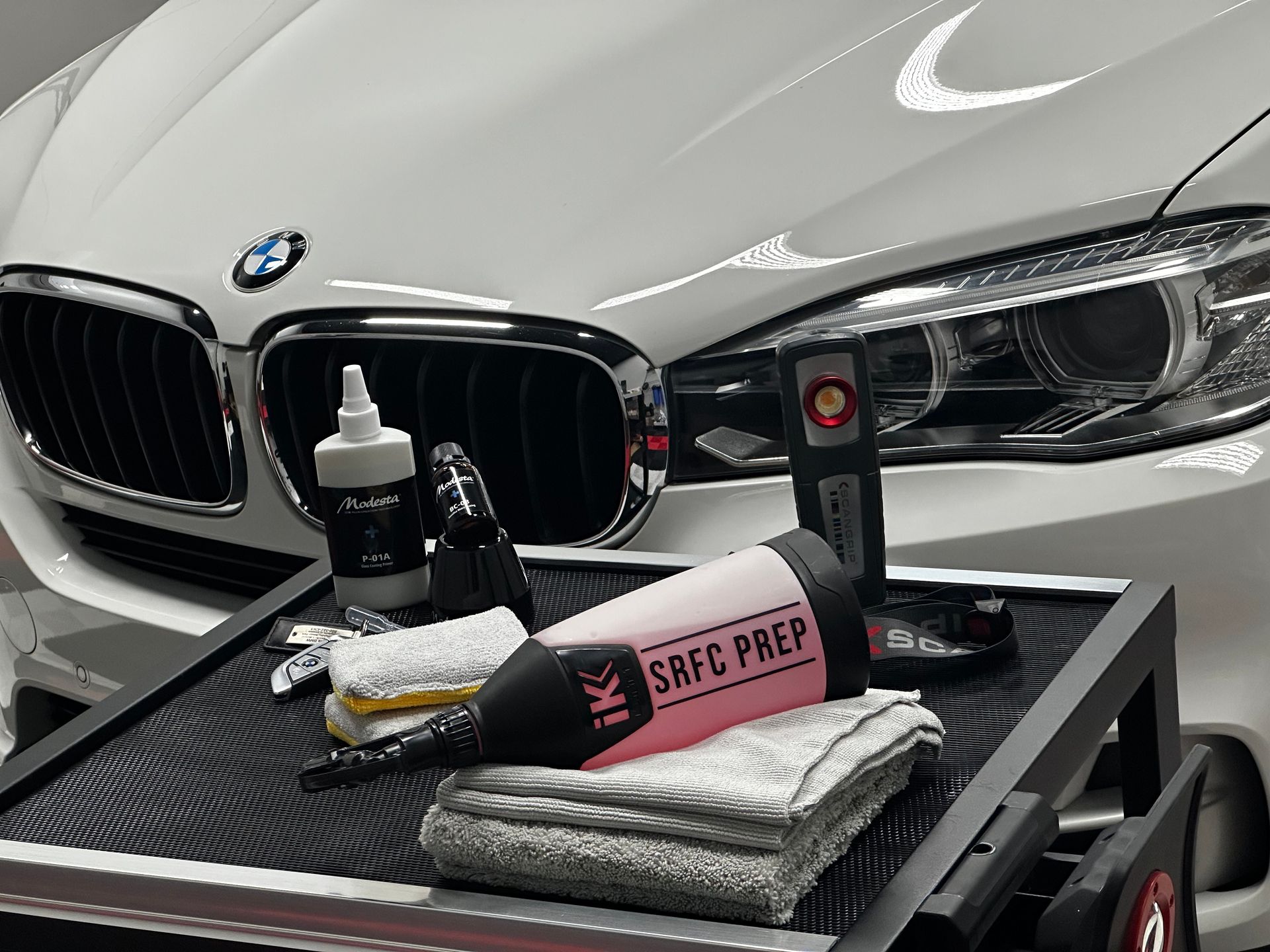 BMW sedan with car detailing supplies on a carbon-fiber tray in front of the grille
