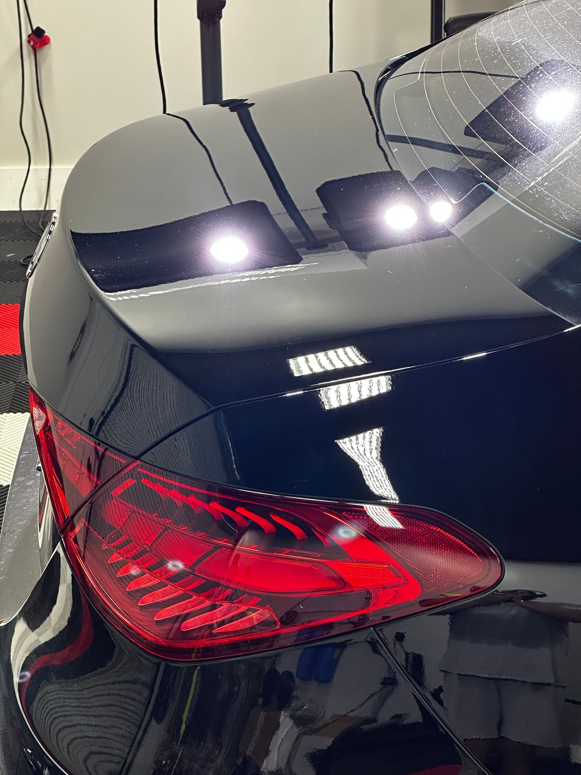 Rear of a black sports car with red taillights and bright reflections in a garage