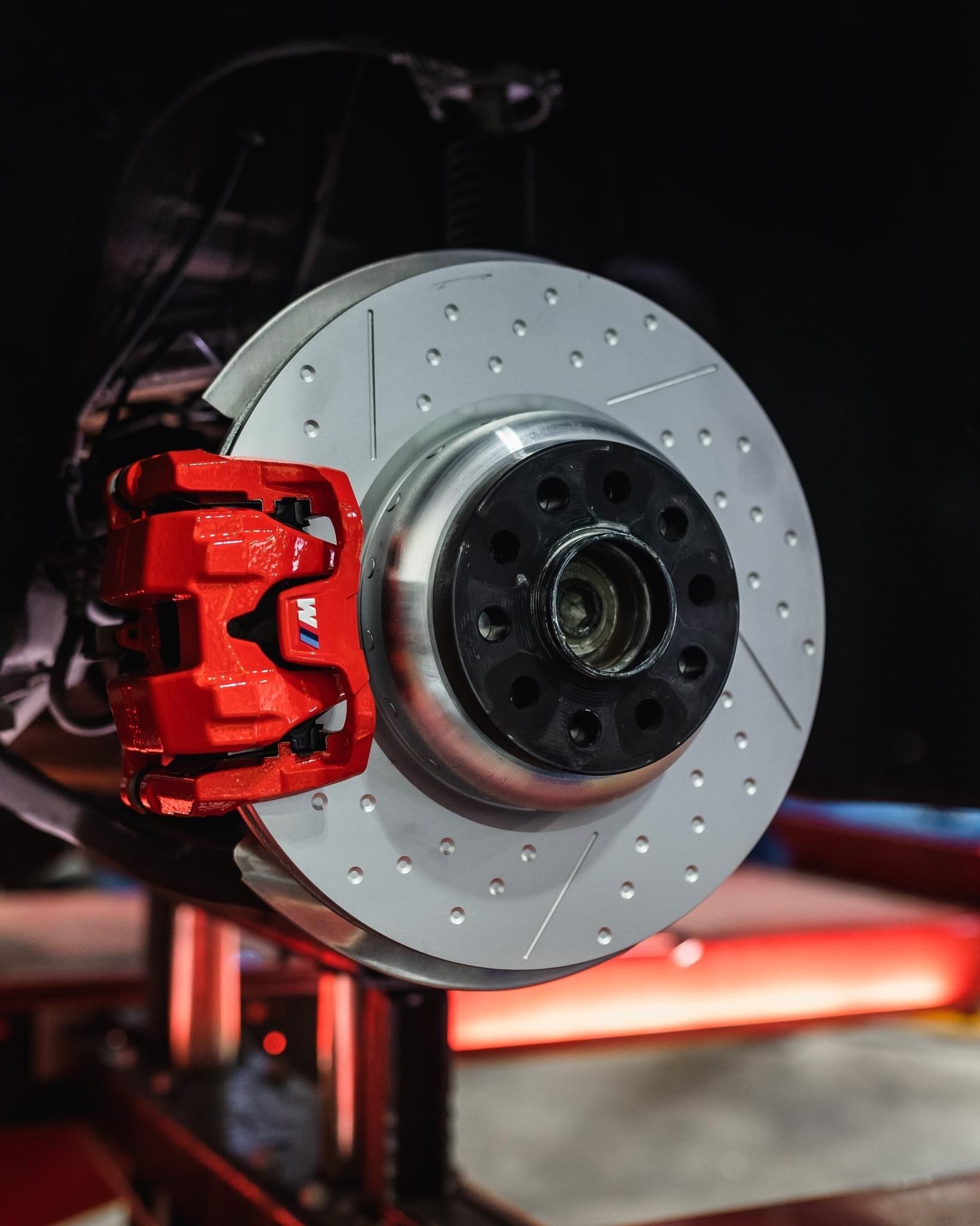 Close-up of a red brake caliper and drilled disc rotor on a car wheel assembly.