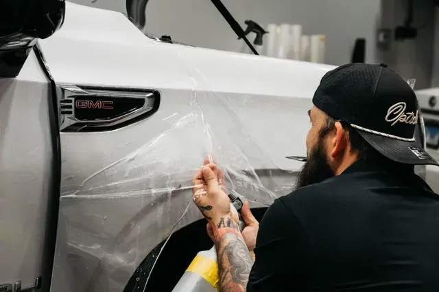Man applying clear film to a white car door in a workshop
