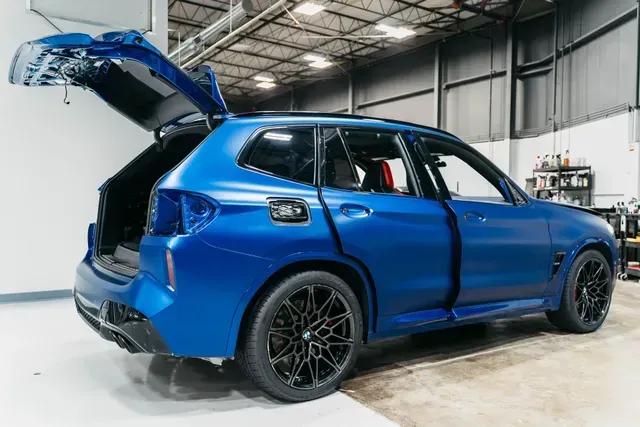 Blue SUV with its rear hatch open in a garage, showing damage along the side.