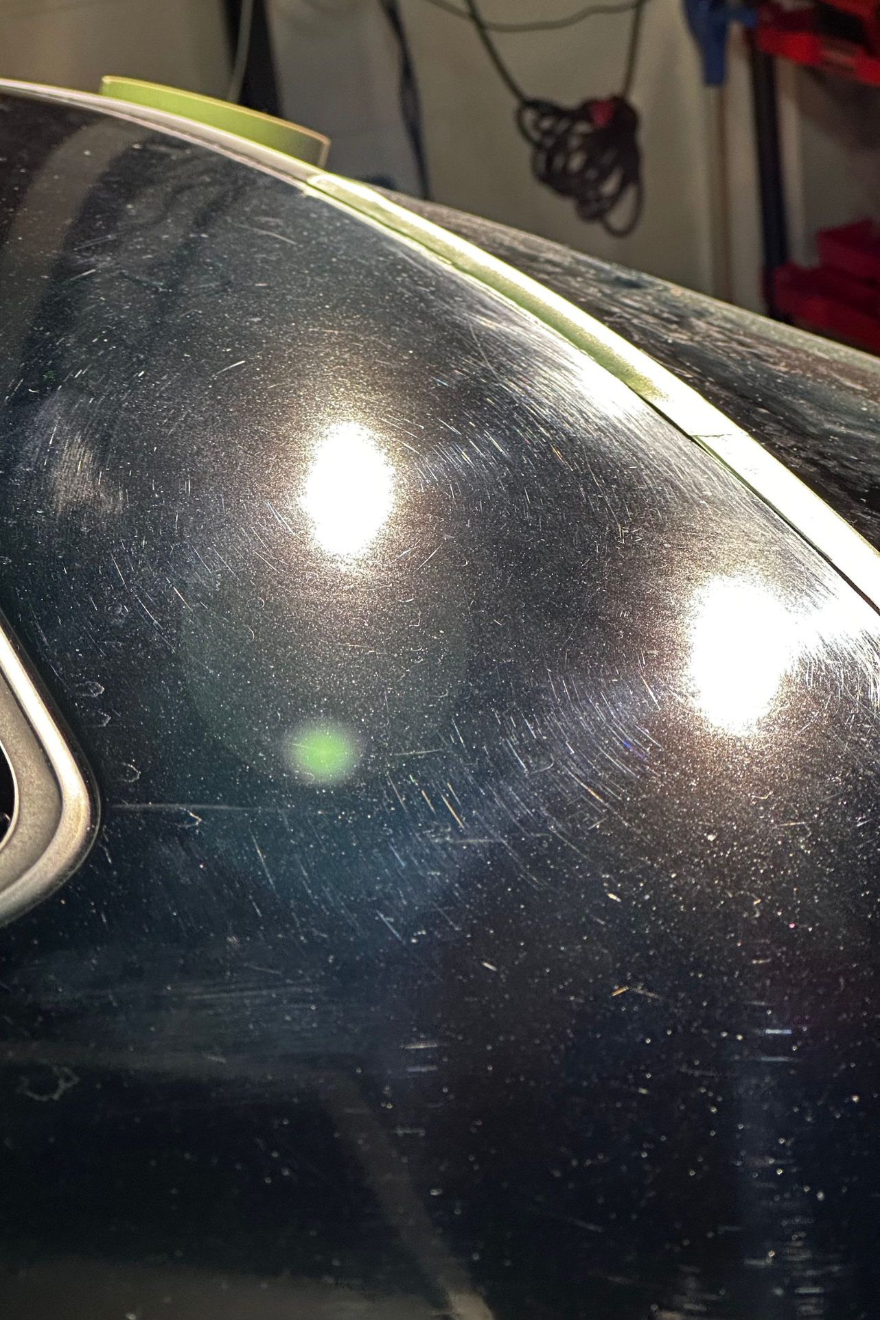 Close-up of a dark car door with metallic speckled paint reflecting bright lights.