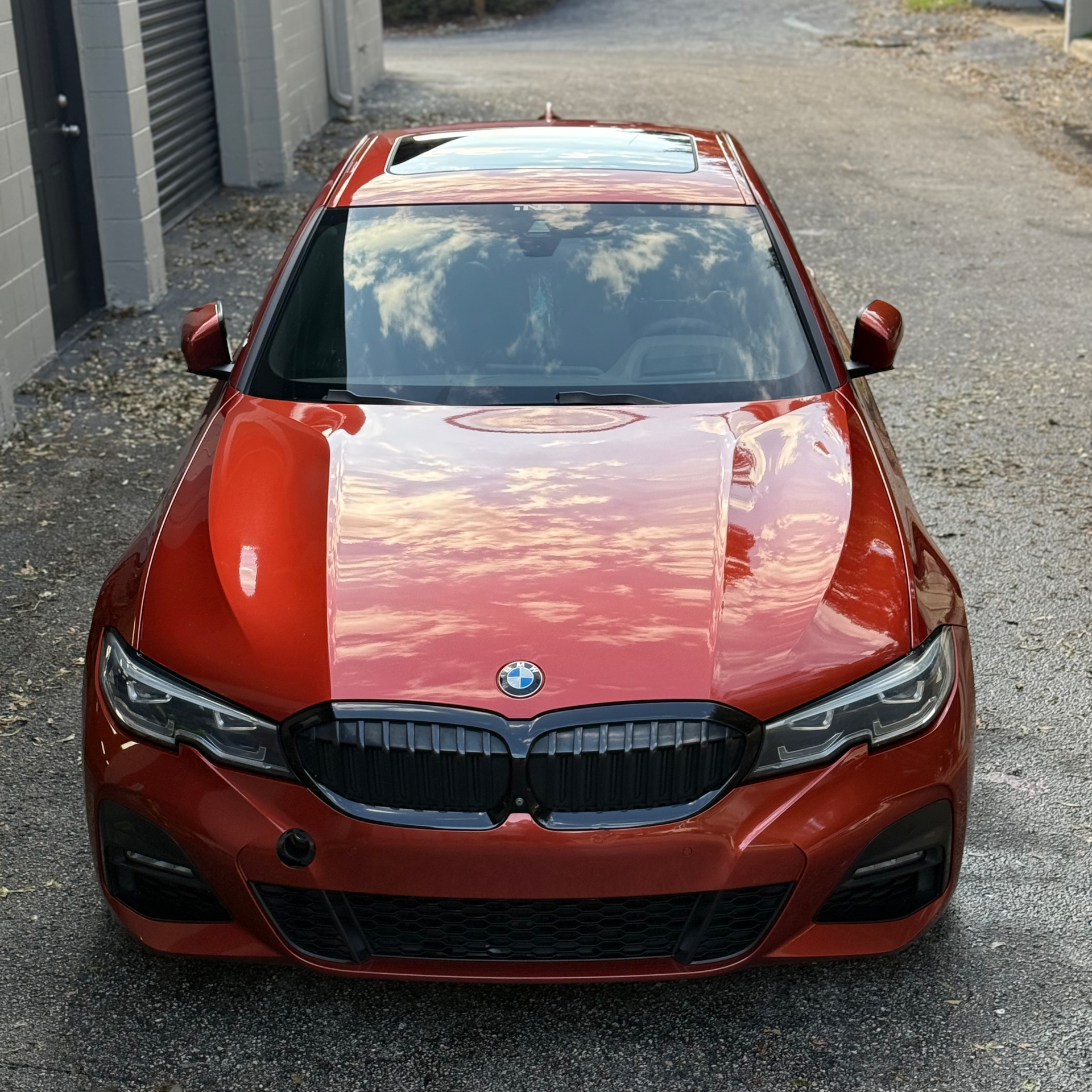 Red BMW sedan parked outdoors, front view, with glossy paint reflecting the sky.