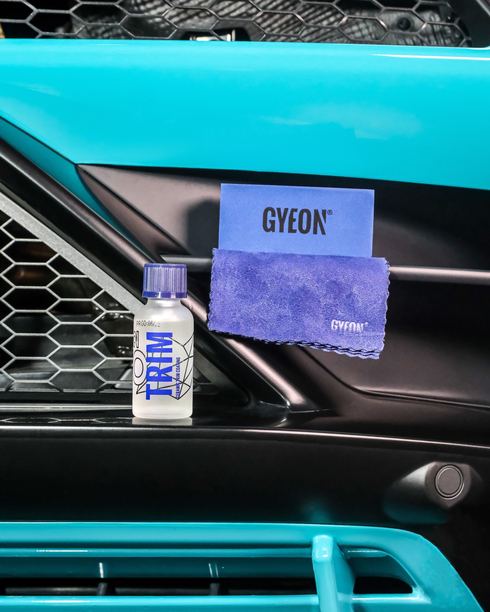 GYEON microfiber applicator and bottle beside a teal car grille trim