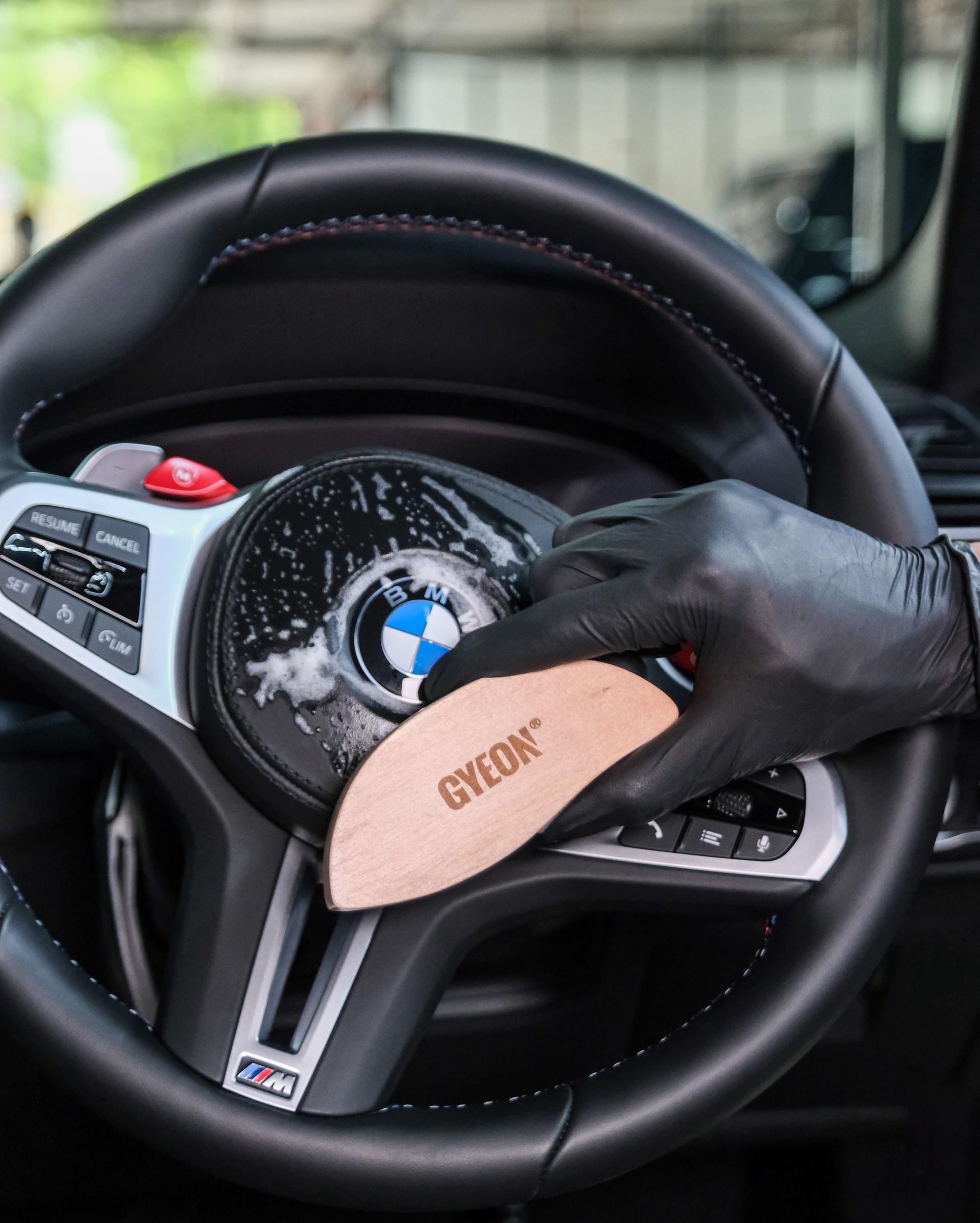 Black-gloved hand holding a beige object with BMW logo against a car steering wheel