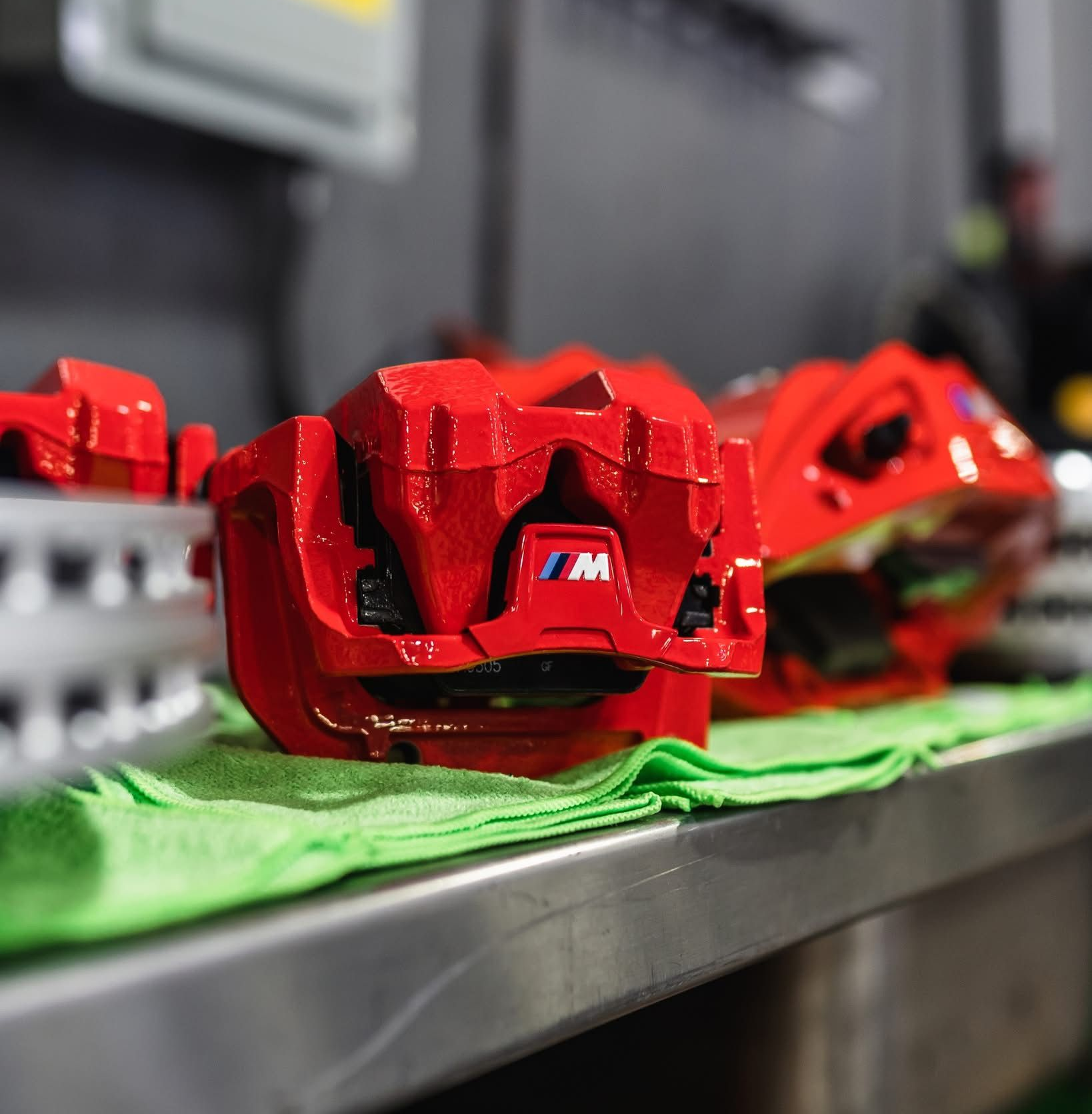 Red brake calipers lined up on a workbench, with one in focus on a green cloth.