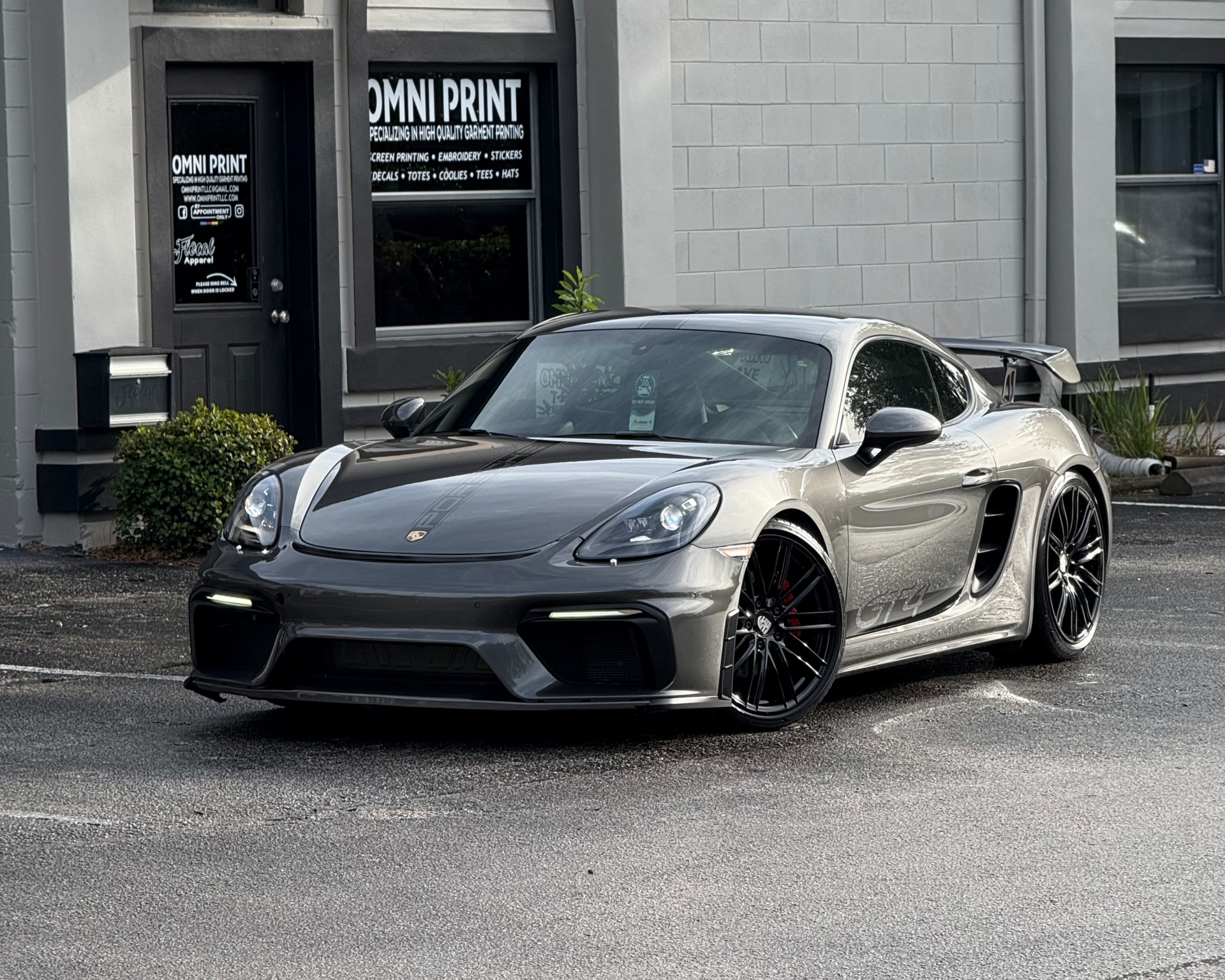 Black sports car parked outside a building with glass windows on a wet street.