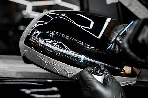 Gloved hands removing protective film from a glossy black car part in a workshop