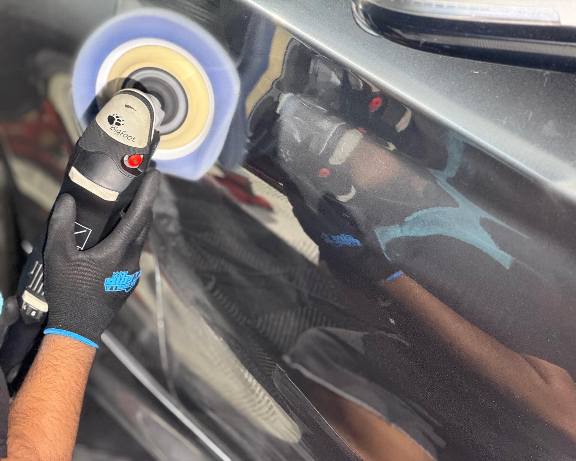 Person polishing a black car with a power buffer, creating a glossy finish