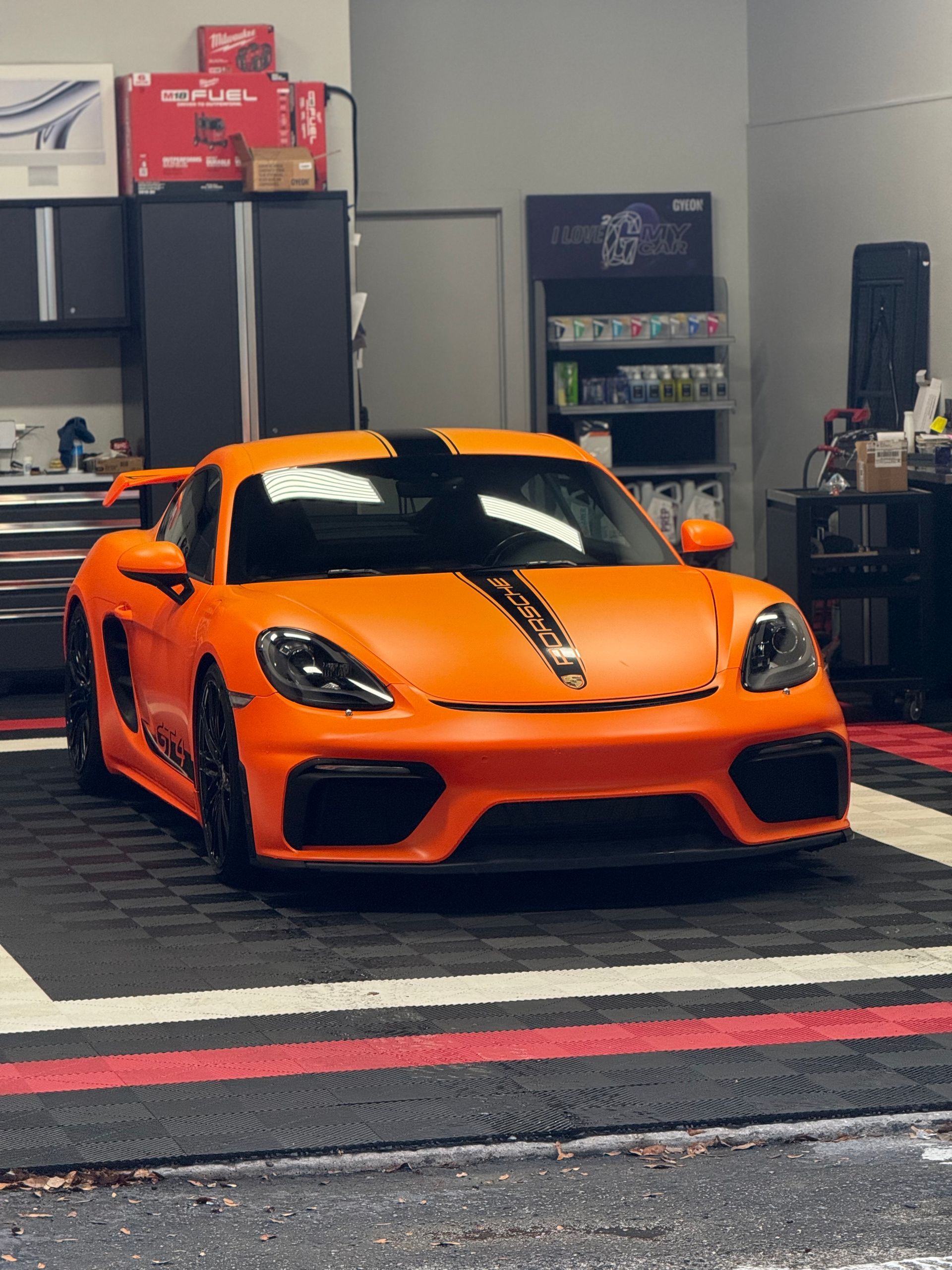 Orange sports car parked indoors in a garage, front view with black racing stripe
