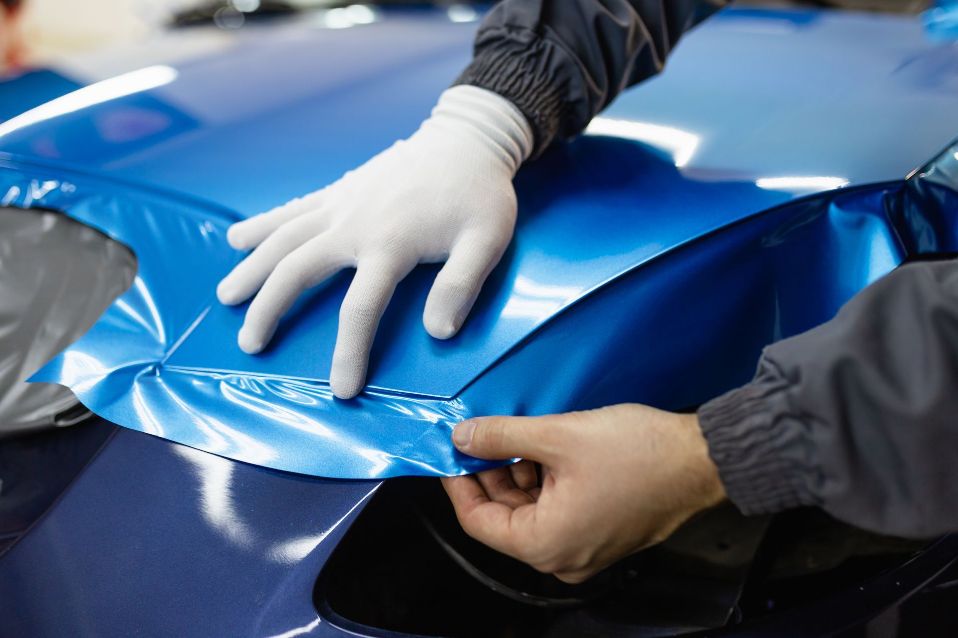 Gloved hands peeling blue protective film from a car hood