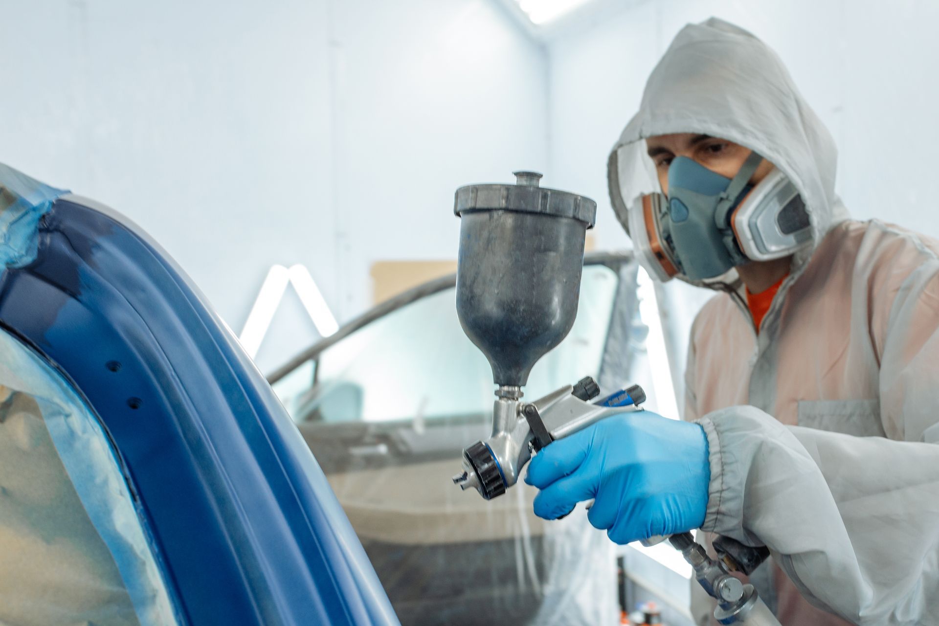 Person in protective gear spray-painting a car in an auto body shop