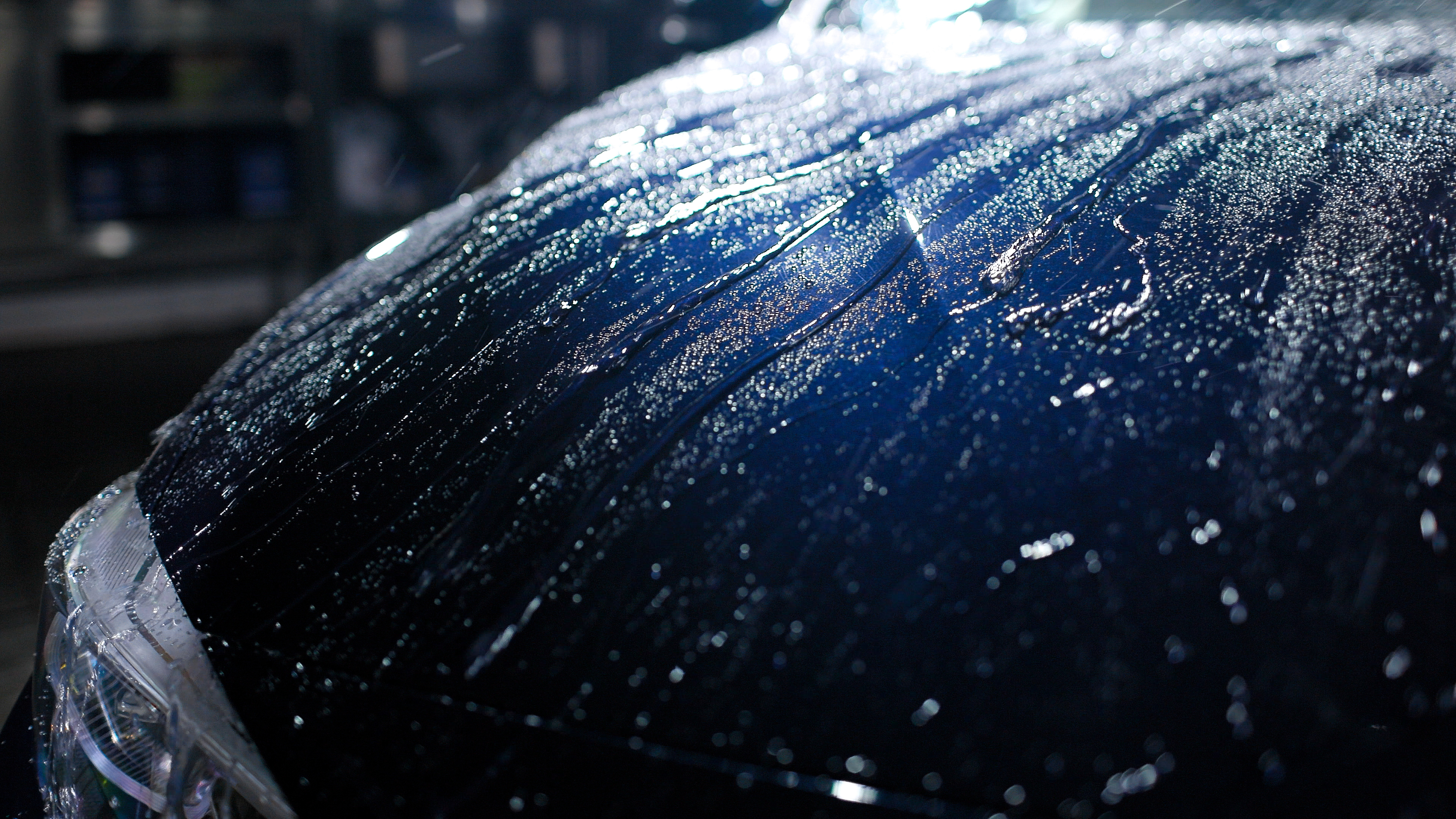 Rain-soaked dark car hood with water droplets glistening under city lights