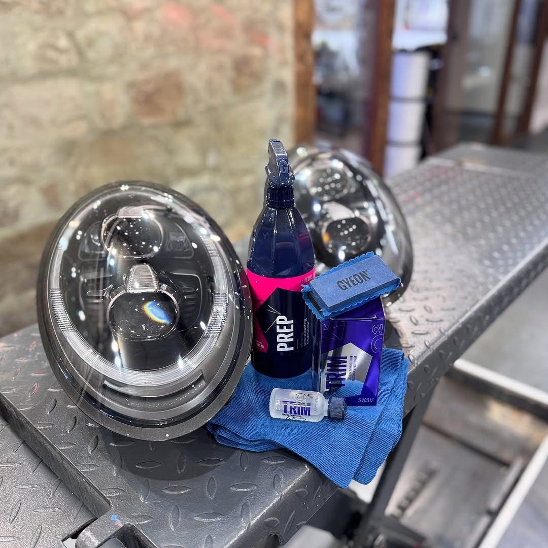 Two chrome car headlamps, detailing spray, and cleaning cloth on a metal workbench