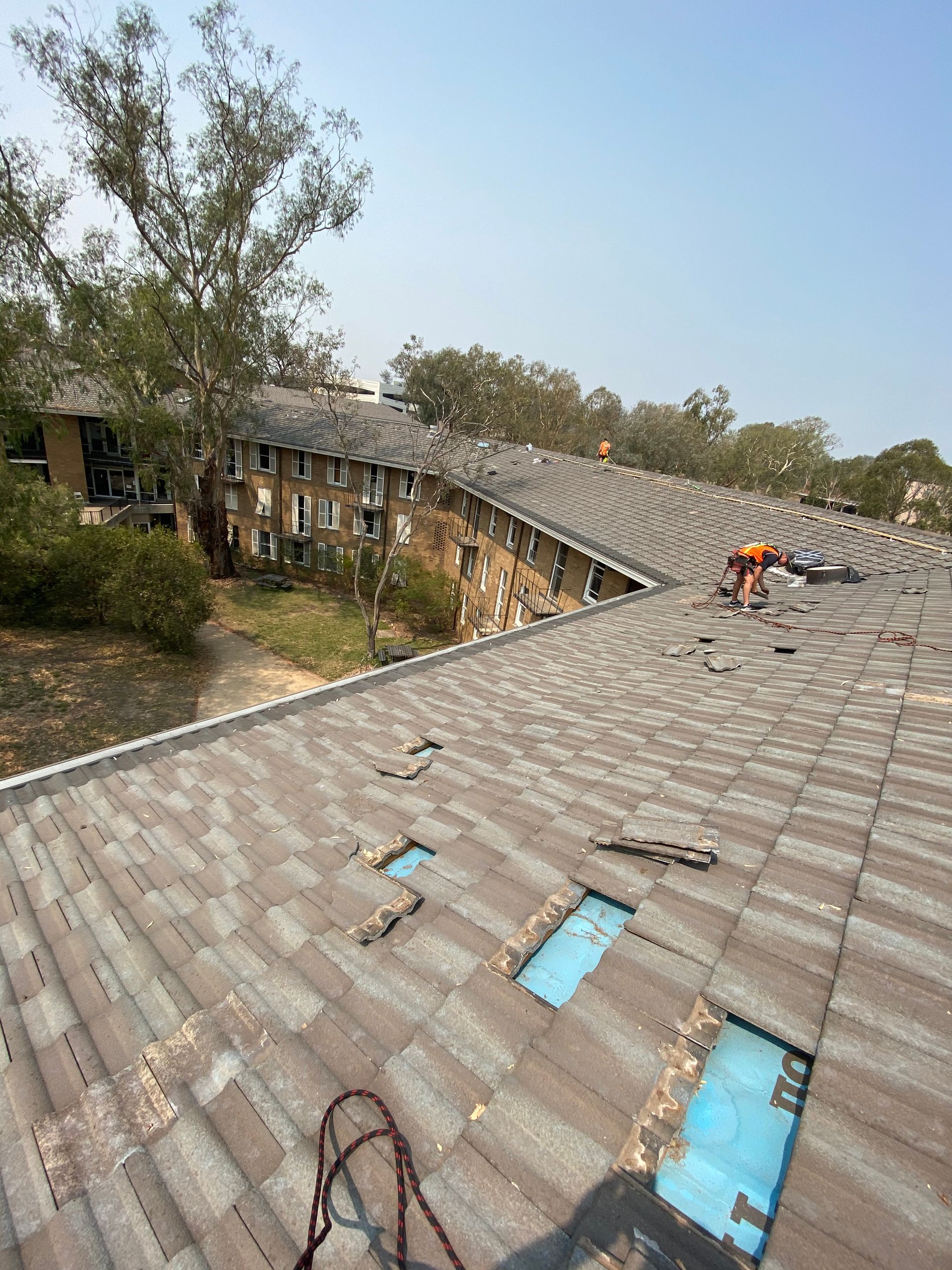 Roof with missing shingles, exposing blue underlayment; worker repairs the damaged section. — Boostn Pty Ltd in Tin Can Bay, QLD