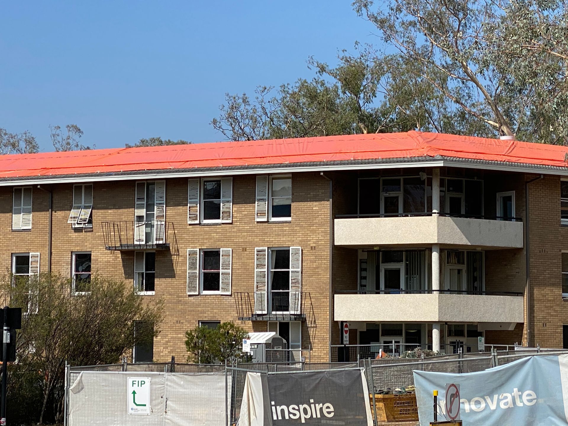 Three-story brick building with orange roof, white shutters, and construction fencing in front. — Boostn Pty Ltd in Tin Can Bay, QLD
