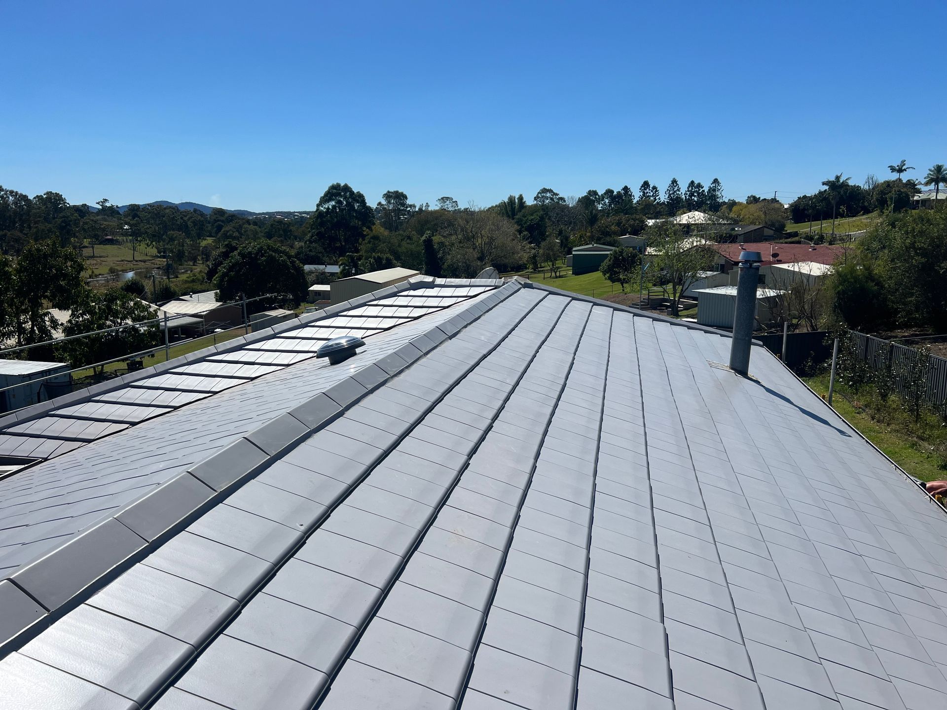 Gray metal roof with blue sky, trees, and buildings in the background. — Boostn Pty Ltd in Tin Can Bay, QLD