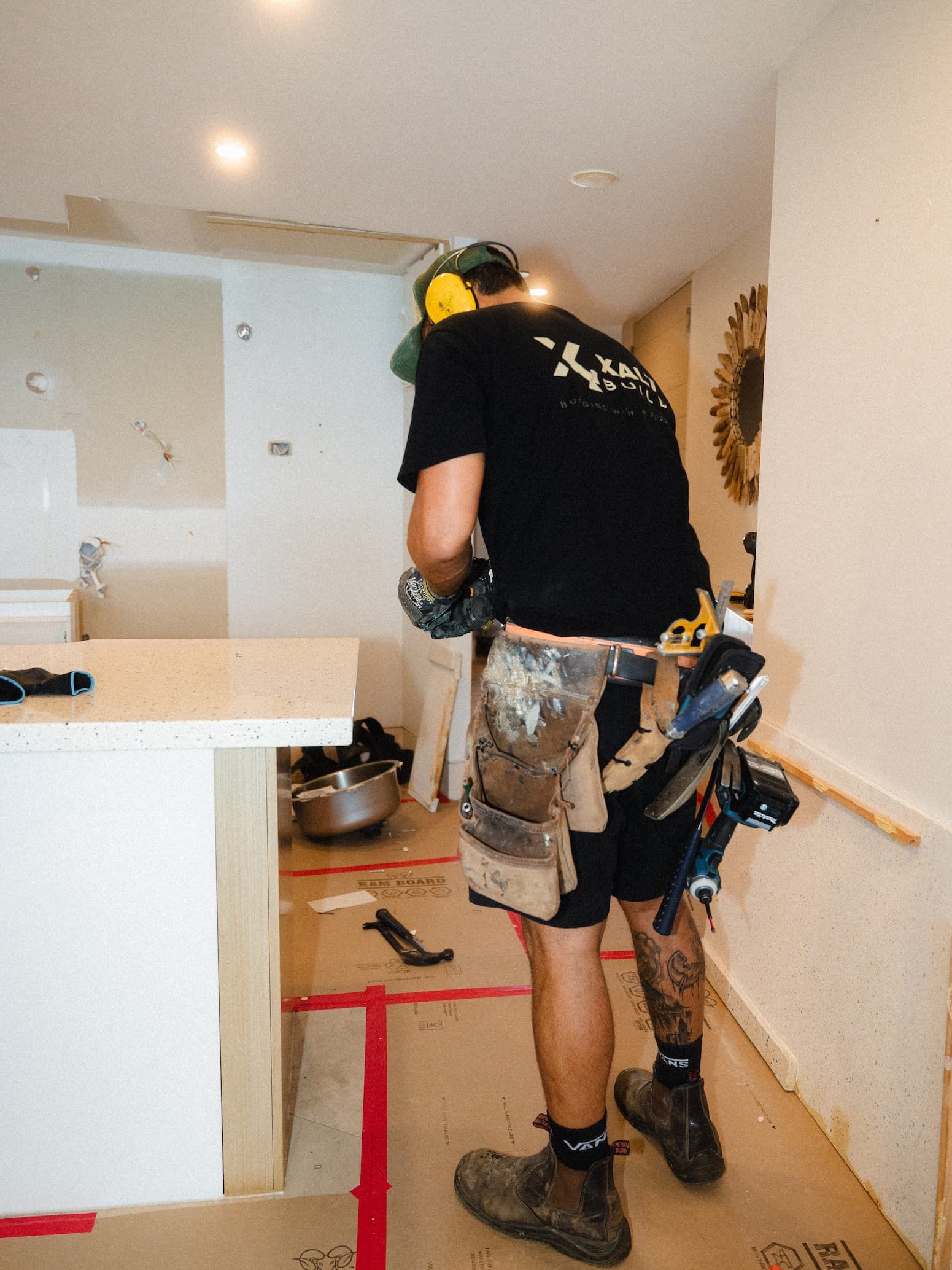 Person standing on a kitchen counter, working on a wall above a red step stool and tools.