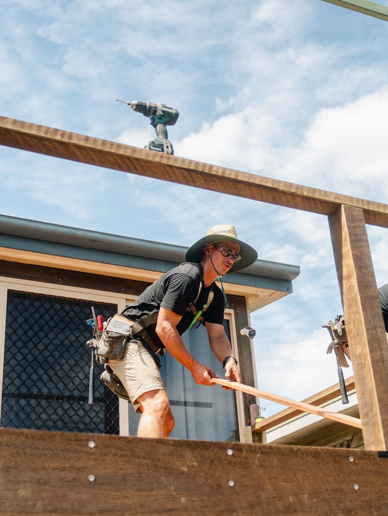 Construction worker hammering wood framing on a house exterior under a blue sky