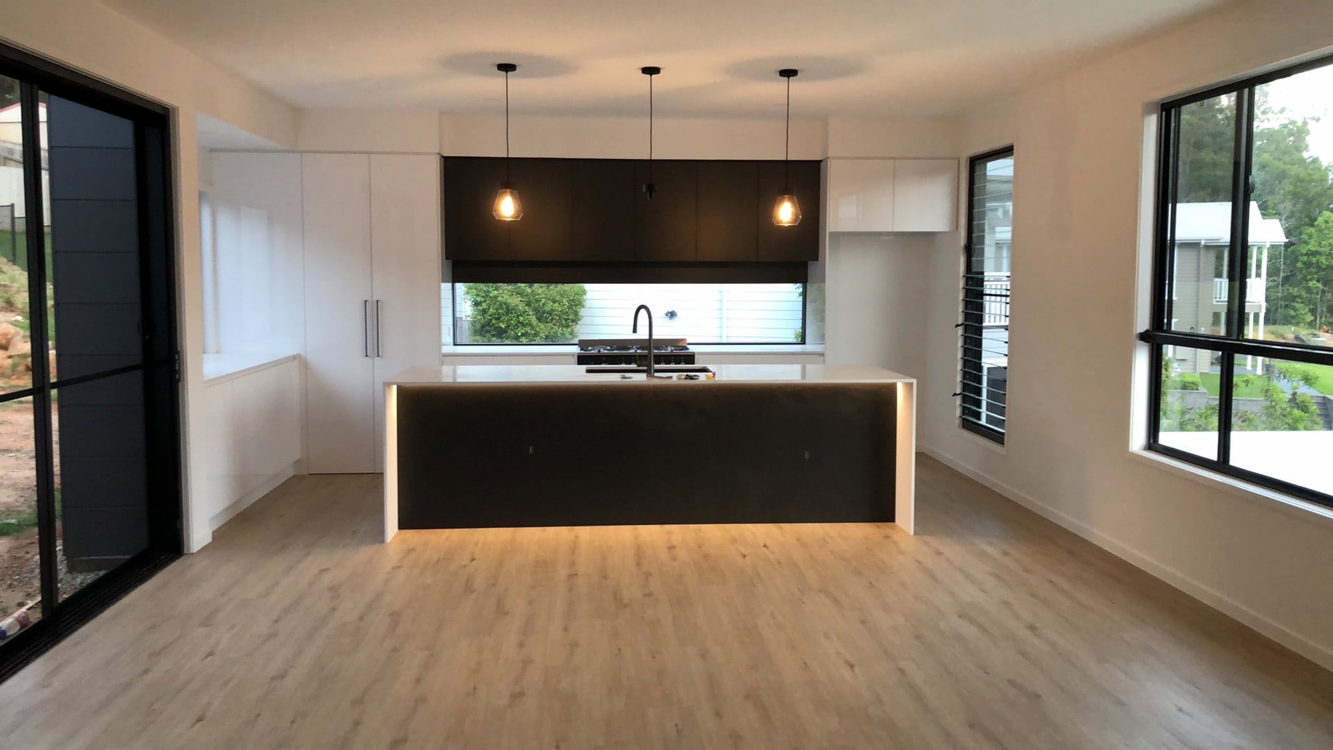 Modern kitchen with dark island, white cabinetry, light wood floors, and large windows.
