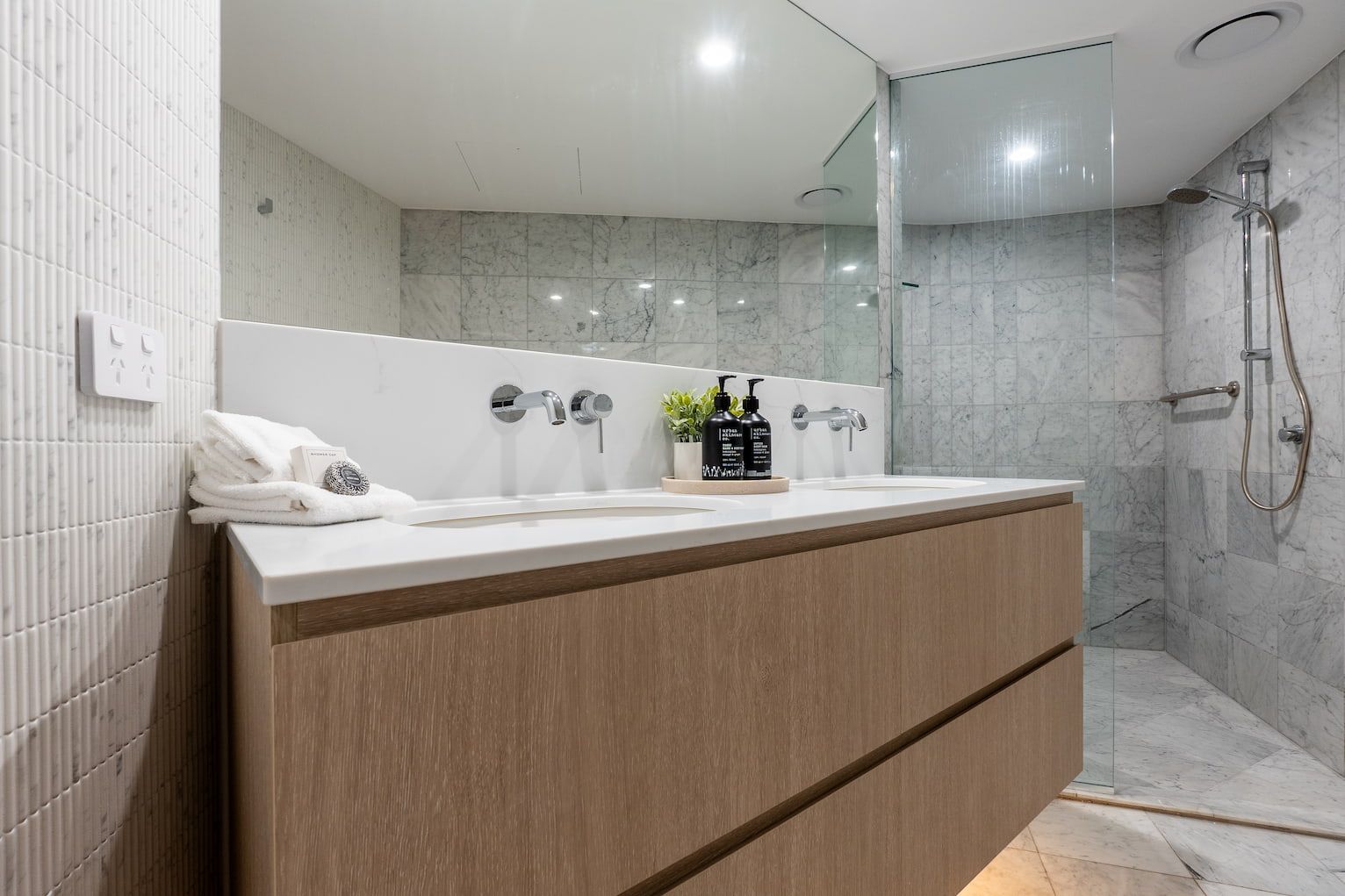 Modern bathroom with wood vanity, white sink, large mirror, and glass shower enclosure