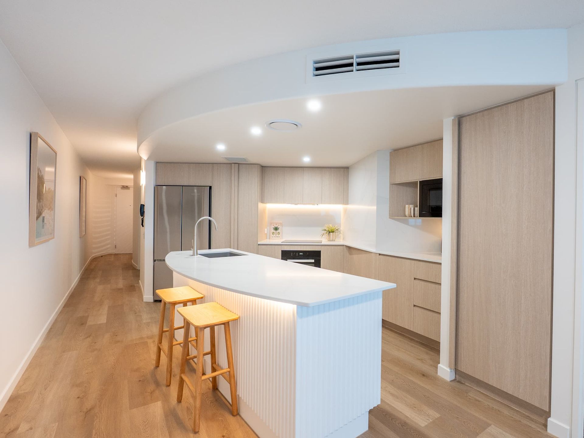 Modern open-plan kitchen with white island, wood floors, and light wood cabinetry