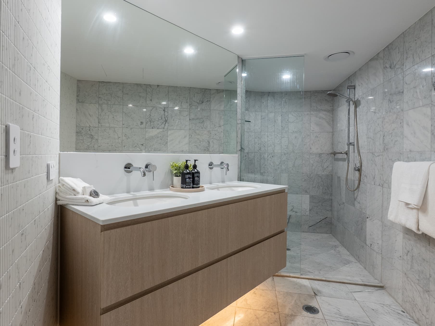 Modern bathroom with double sink vanity, large mirror, and glass-enclosed shower in gray stone tiles