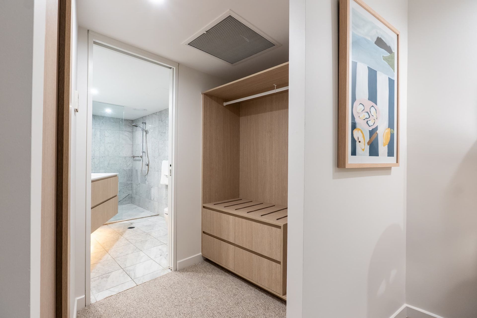 Built-in closet beside a bathroom with wood drawers, mirrored door, and a framed wall print.