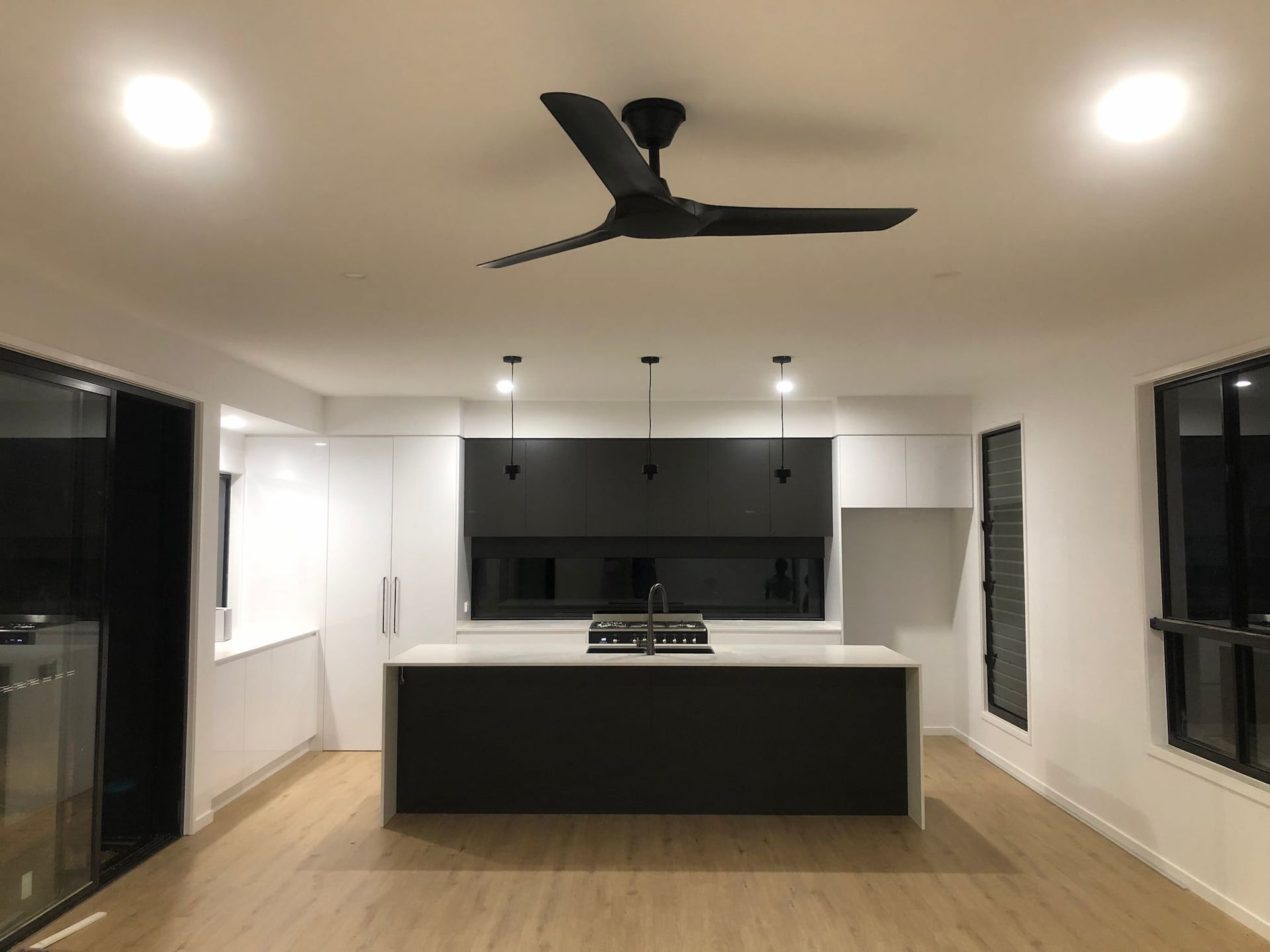 Modern kitchen with white cabinets, dark island, wood floor, and black ceiling fan in an open room