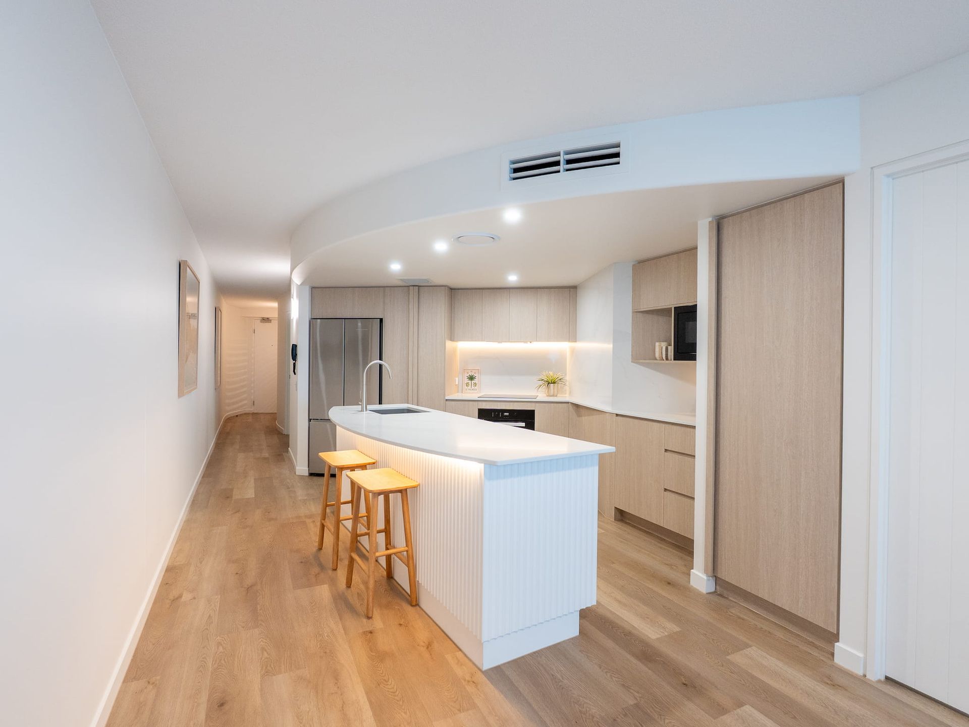 Bright modern kitchen with white island, wood flooring, bar stools, and recessed lighting