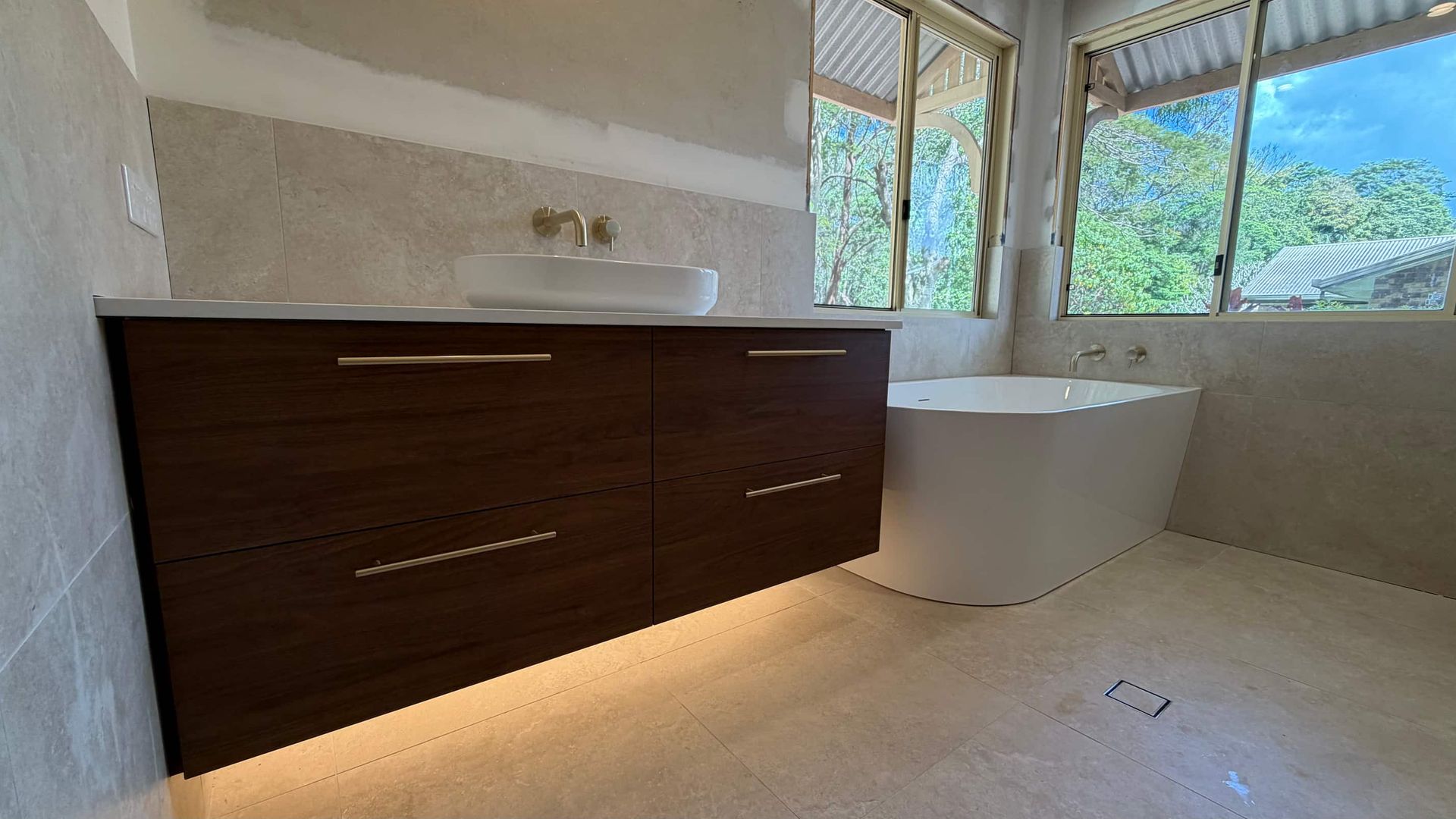 Modern bathroom with dark wood vanity, white bathtub, and large window overlooking greenery