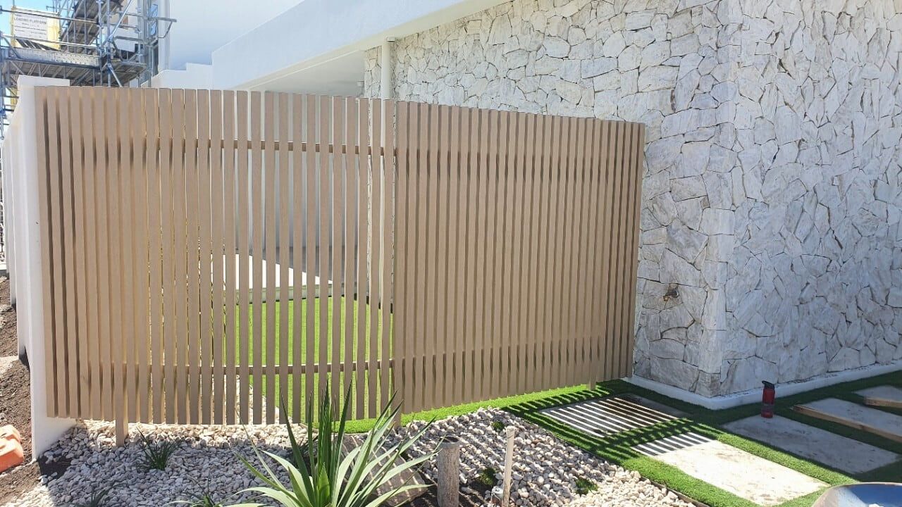 Wooden slat fence beside a stone wall and green lawn in bright sunlight