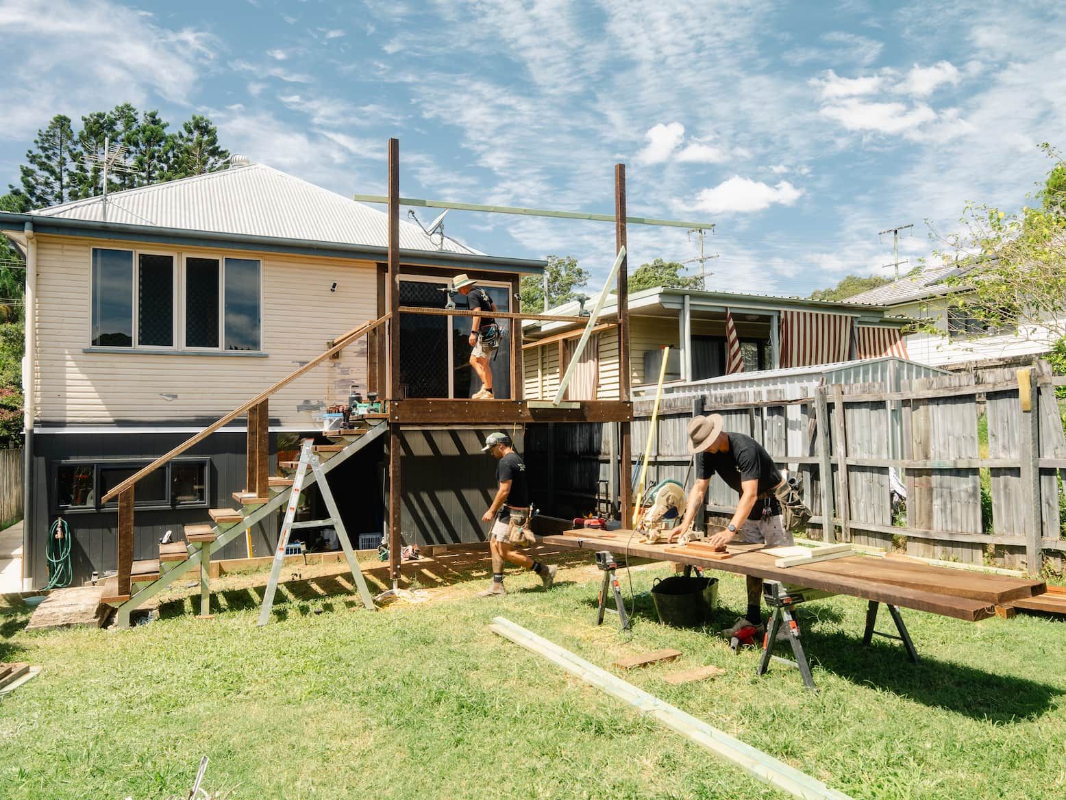 Backyard house renovation with workers building a raised deck and stairs