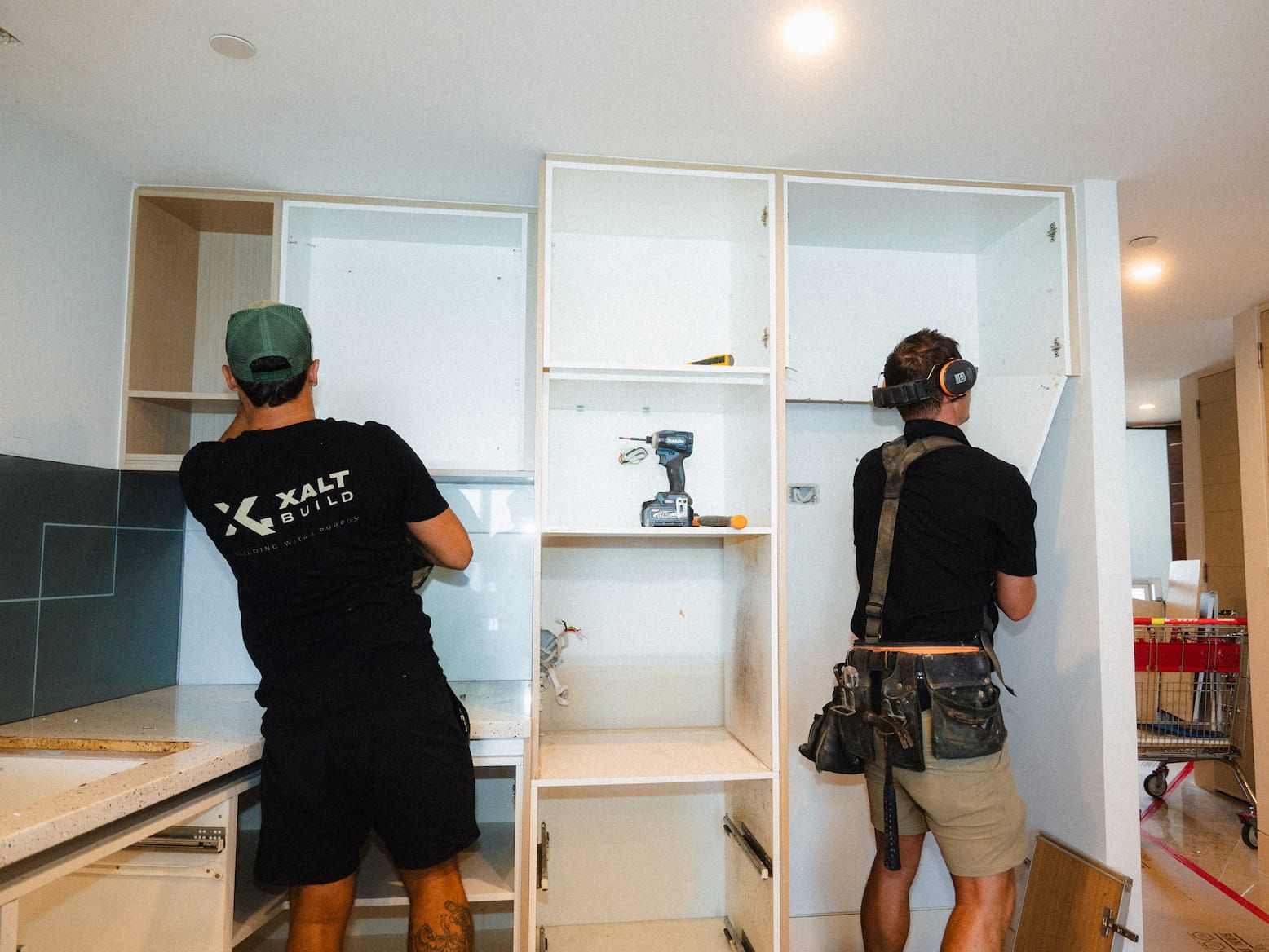 Two workers installing white cabinets in a bright kitchen.