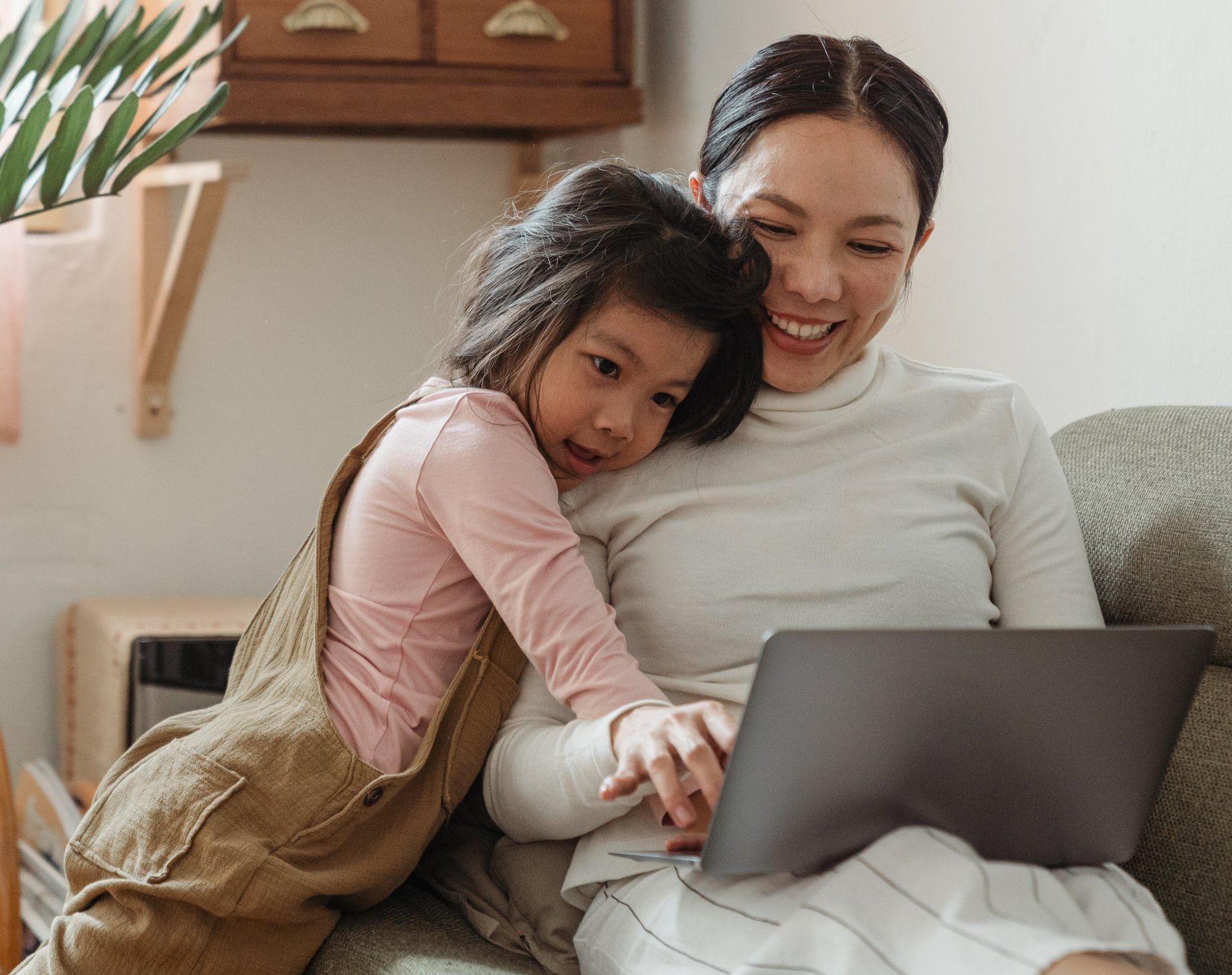 A woman and a little girl are sitting on a couch looking at a laptop.