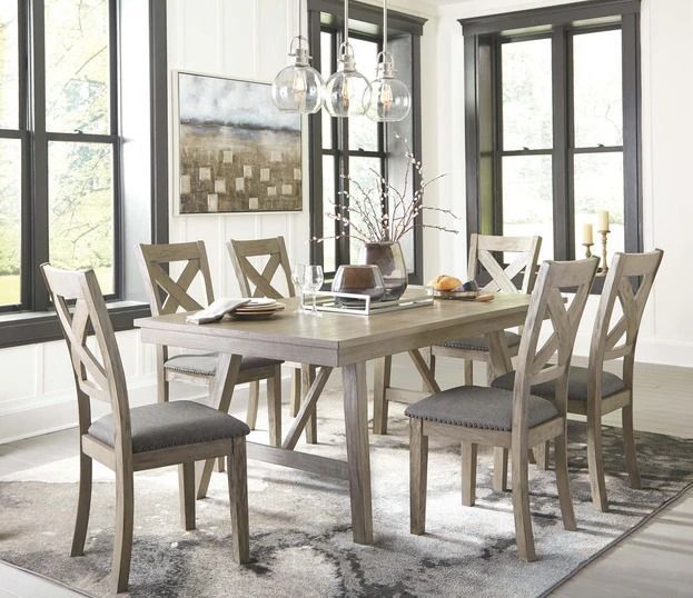 Dining room with light wood table, chairs, and art, featuring a rug and window light.