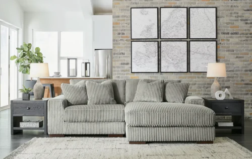 Gray corduroy sectional sofa in a living room with art on the brick wall and two end tables.
