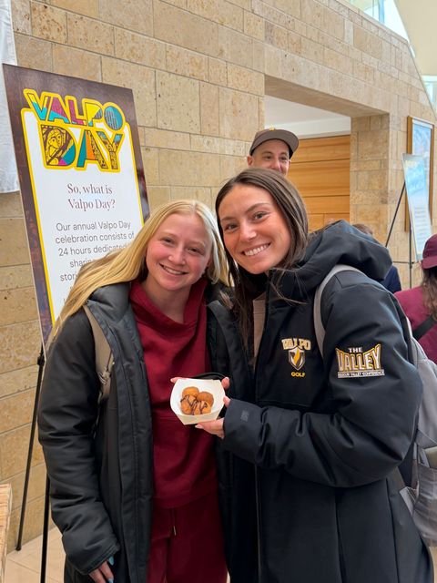 Two people sanding together, smiling and holding donut holes.