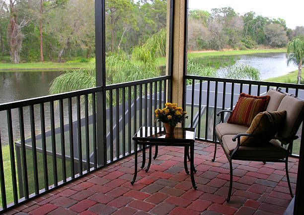 Screened porch overlooking a lake with furniture: loveseat, table, and flowers. Brick floor.