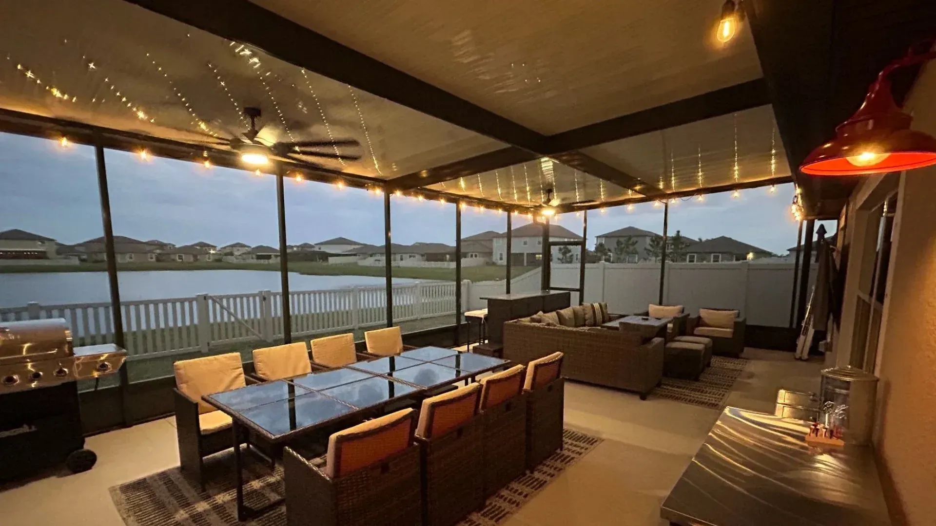 Screened-in patio overlooking lake, with dining table, seating, and string lights.