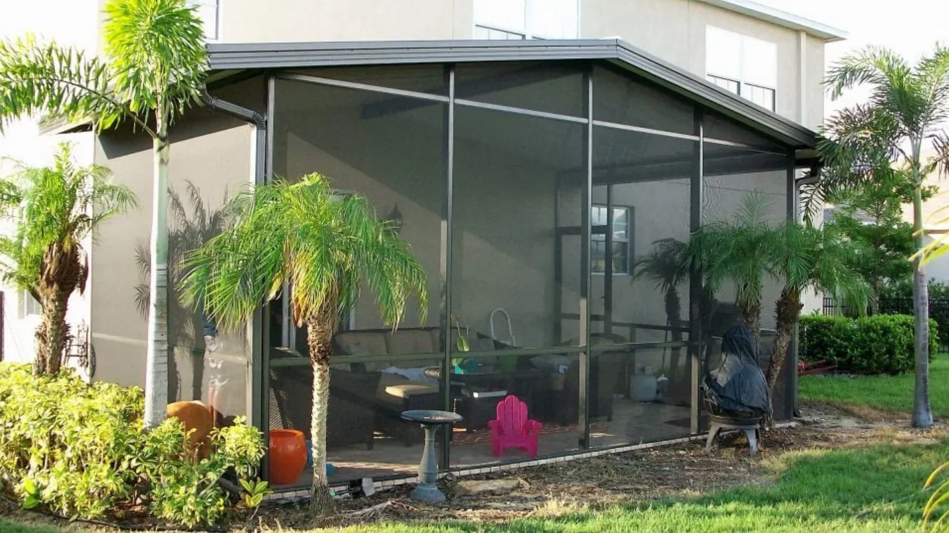 Screened-in patio with dark roof, palm trees, and outdoor furniture.