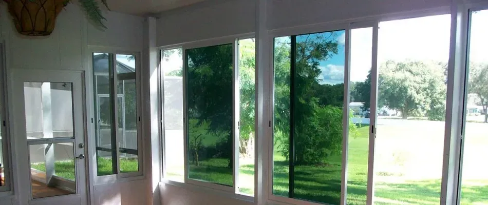Sunroom with multiple pane windows, tinted blue-green, overlooking a grassy yard with trees.