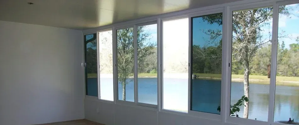 Interior of a room with large windows overlooking a lake and trees, with blue-tinted glass.