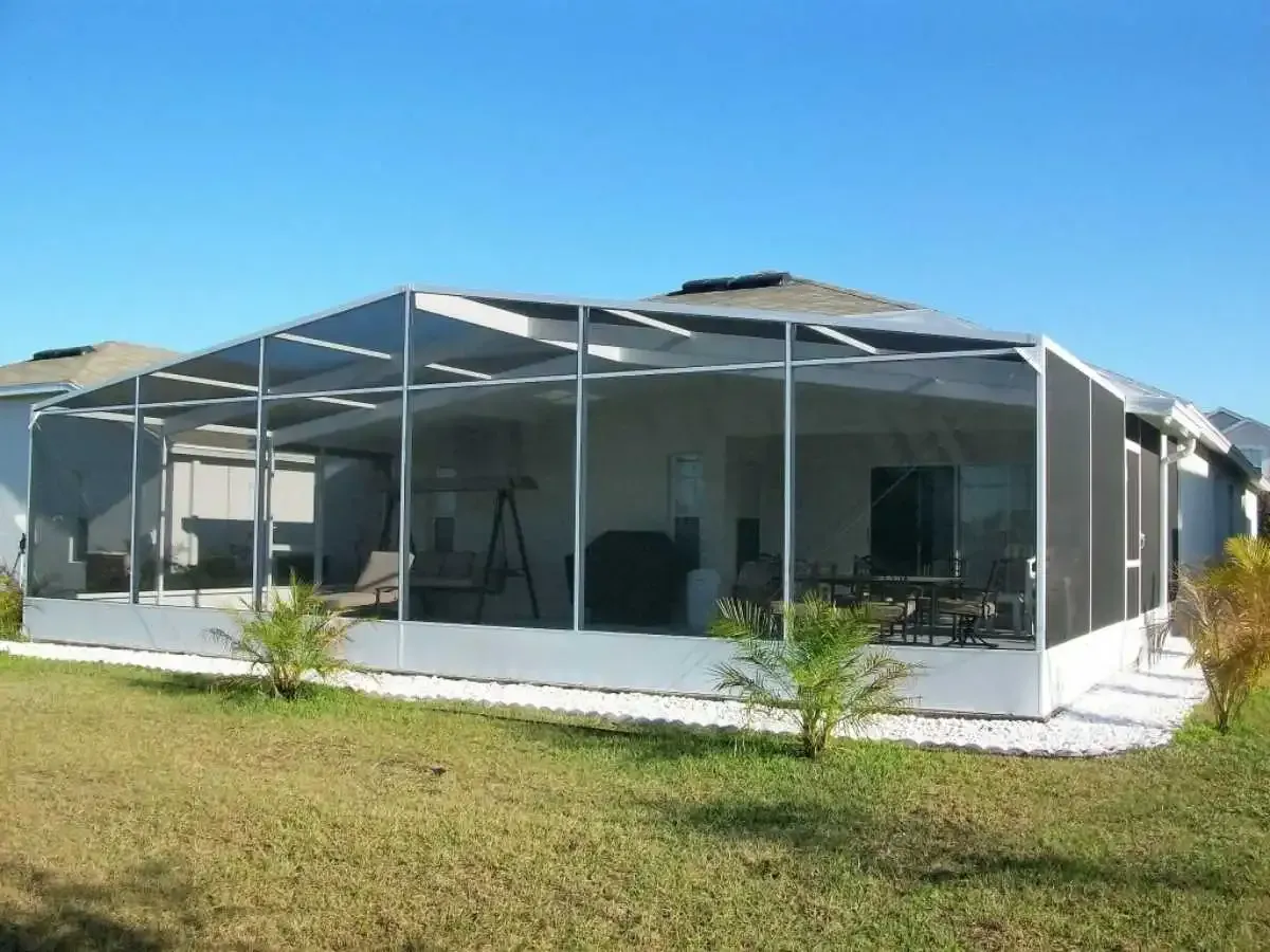 Screened-in patio extension attached to a house with white trim, green lawn, and clear blue sky.